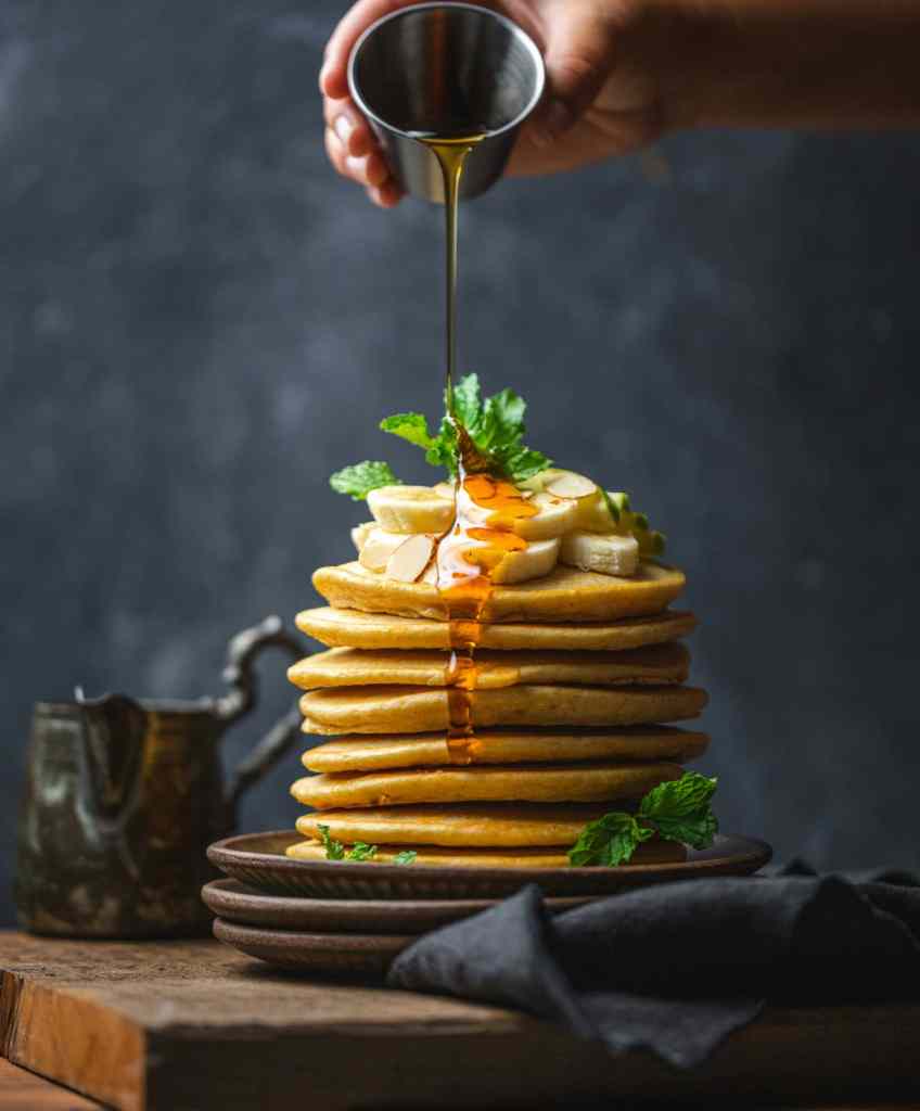 A stack of pancakes with a hand drizzling syrup on top